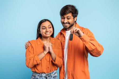 Ein fröhliches indisches Paar hält aufgeregt einen Satz Autoschlüssel in der Hand, der darauf hindeutet, dass sie ein neues Auto gekauft haben