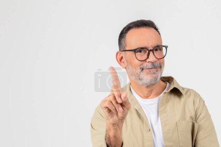 A confident elderly man with glasses pointing upwards with one finger and smiling, set against a white background
