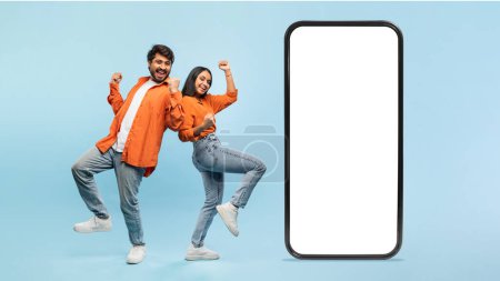 Joven indio hombre y mujer en traje casual posan espalda con espalda con una gran ilustración de un teléfono móvil con una pantalla en blanco para maqueta