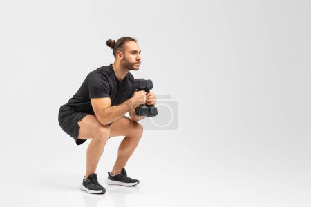 Hombre determinado en traje de ejercicio realiza una posición de agacharse mientras sostiene pesas