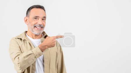 A cheerful elderly man with a beard smiles and points to the side, standing against a white background