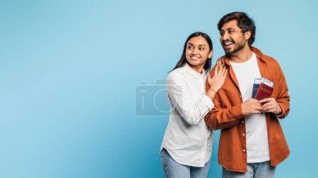 Photo for Hindu man and woman hold passports and look to the side with curious expressions, suggesting travel or adventure - Royalty Free Image