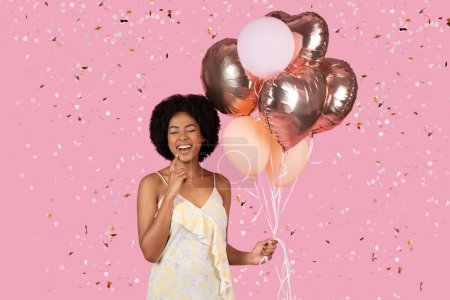 Excited African American woman with a mixture of pink and heart-shaped balloons among falling confetti