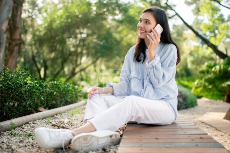 Téléchargez les photos : Une femme profite d'une agréable conversation téléphonique dans le parc, incarnant le confort de la communication mobile - en image libre de droit