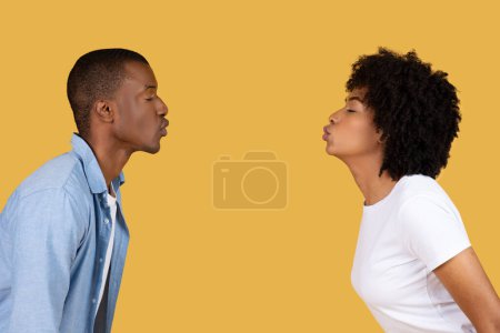 Photo for A man and woman stand facing each other in profile with a plain yellow background, African American couple kissing - Royalty Free Image