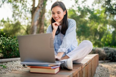 Photo for A focused woman studies with a laptop and books, blending outdoor relaxation with productivity and learning - Royalty Free Image