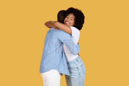 Das junge afroamerikanische Paar umarmt sich herzlich, und die Frauen lächeln strahlend, als sie den Mann vor gelbem Hintergrund umarmt
