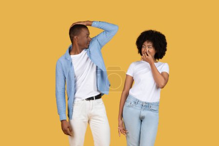 Foto de Hombre y mujer afroamericanos están de pie juntos, reaccionando a un mal olor con las narices arrugadas sobre un fondo amarillo - Imagen libre de derechos