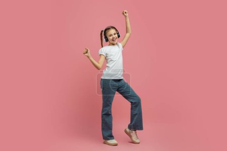 Téléchargez les photos : Une fille aime la musique avec des écouteurs tout en dansant, montrant un mouvement dynamique sur fond rose, pleine longueur - en image libre de droit