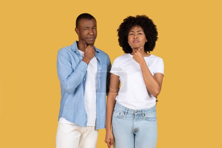 Foto de Hombre y mujer afroamericanos parecen pensativos, tocando sus barbillas, mirando a un lado sobre un fondo amarillo - Imagen libre de derechos