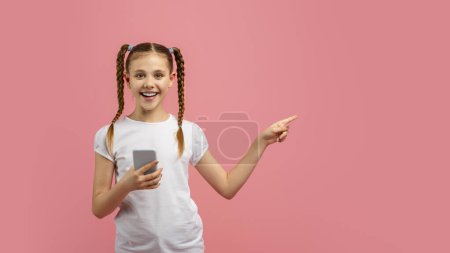 Téléchargez les photos : Une fille souriante avec des tresses tenant un téléphone et pointant quelque chose sur le côté sur un fond rose - en image libre de droit