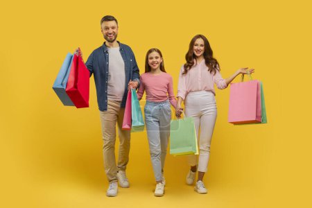 Photo for The image depicts a content family of three walking and holding multiple shopping bags, matching a casual style on yellow - Royalty Free Image