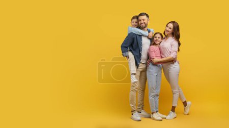 Téléchargez les photos : Une famille très unie se serre les coudes, affichant affection et sourire sur un fond jaune studio ensoleillé - en image libre de droit