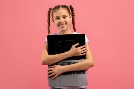 A delighted girl wearing casual clothes hugs a laptop with a blank screen, showing love for technology