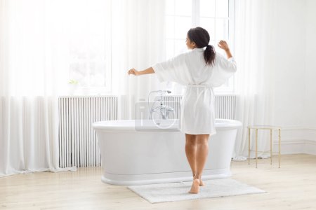 Capturando un momento de dicha, la mujer afroamericana abre sus brazos junto al baño en un baño prístino y decorado con blanco