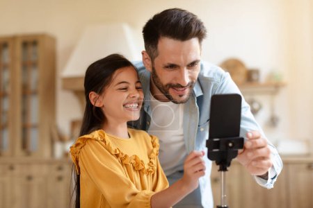 Vater und Tochter halten einen lustigen Vlogging-Moment mit dem Smartphone auf einem Stativ fest und teilen ihre Kreativität