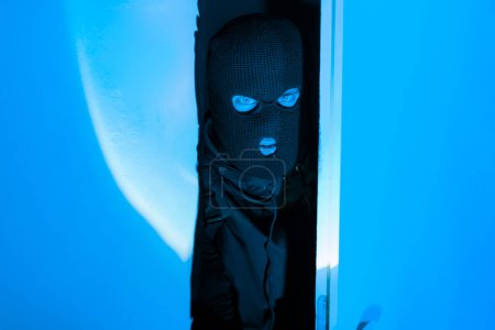 Téléchargez les photos : Un voleur masqué prudent qui regarde à travers avec une expression tendue suggérant un danger imminent ou une opération secrète dans l'obscurité - en image libre de droit