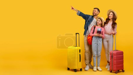 Téléchargez les photos : Une famille heureuse avec des bagages pointant vers quelque chose au loin, prêt pour le voyage et l'aventure, espace de copie - en image libre de droit