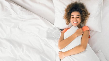 Téléchargez les photos : Jeune femme étreignant l'oreiller au lit, profitant de l'heure du matin, vue sur le dessus - en image libre de droit