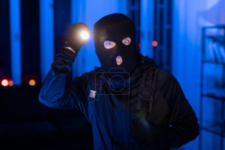 Une image intense représentant un intrus avec une lampe de poche fouillant une pièce, moulée dans une teinte bleue pour un look cinématographique