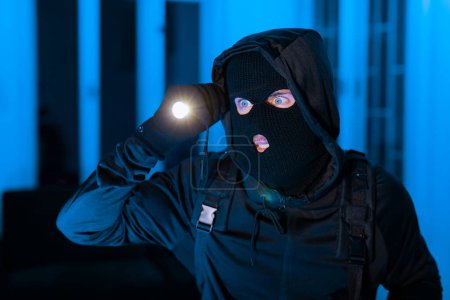 Ein einprägsames Bild eines Einbrechers, der intensiv mit einer Taschenlampe sucht, was die Fokussierung krimineller Durchsuchungen unterstreicht