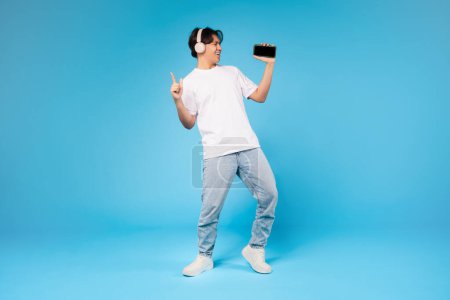 Un exuberante joven asiático escucha música y baila con su teléfono inteligente, que representa el ocio y el uso de la tecnología