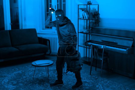 Foto de Una figura misteriosa con una linterna explora una habitación bañada en luz azul, la atmósfera es tensa e intrigante - Imagen libre de derechos