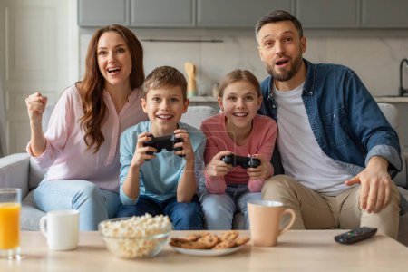 Familia de cuatro personas enfocadas y comprometidas mientras juegan videojuegos en un cómodo sofá en el interior del hogar