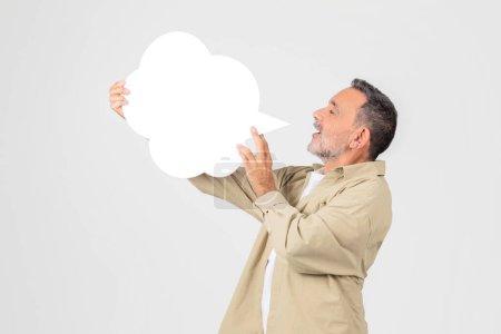 Photo for A senior man interactively holding out a blank speech bubble, suitable for customizable messages or text - Royalty Free Image