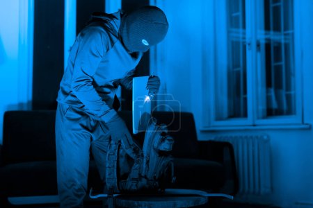 Photo for A cloaked figure organizes tools, preparing for a break-in, with a sinister lamp illumination suggesting an upcoming crime - Royalty Free Image