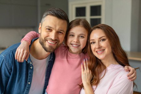 Eine fröhliche dreiköpfige Familie mit einem jungen Mädchen, das sich in einer hellen Wohnküche umarmt und Wärme und Zusammengehörigkeit vermittelt