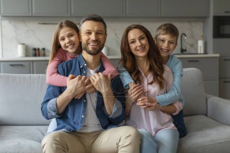 Porträt einer lächelnden Familie mit zwei Kindern, die gemütlich auf einem Sofa im gemütlichen Wohnzimmer sitzt