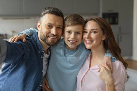 Photo for A cheerful family of three with a young boy smiling for a camera selfie, in a cozy home environment - Royalty Free Image