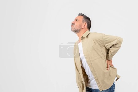 Photo for Man exhibits a stance of discomfort or pain, holding his lower back, possibly implying a strain or injury needing attention - Royalty Free Image