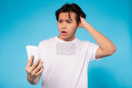 Foto de Adolescente asiático que experimenta sorpresa o shock mientras mira la pantalla de su teléfono inteligente, expresando su incredulidad - Imagen libre de derechos
