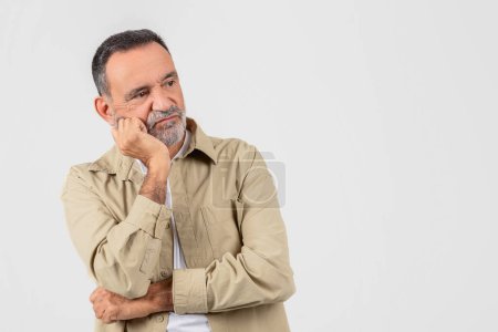 Photo for A senior man with a beard appears contemplative, resting his face on his hand against a white background His expression suggests deep thought or concern - Royalty Free Image