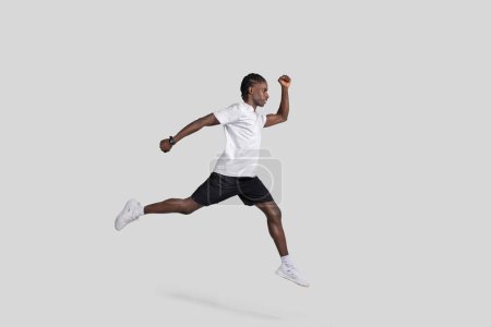 Téléchargez les photos : Image dynamique d'un Afro-Américain capturé dans une pose de course en vol sur un fond gris clair, illustrant le mouvement et l'athlétisme - en image libre de droit