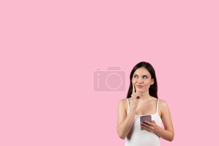 Photo for A contemplative lady holding a cellphone, evokes a European summer feel, perfect for generation z marketing, set against an isolated pink backdrop - Royalty Free Image