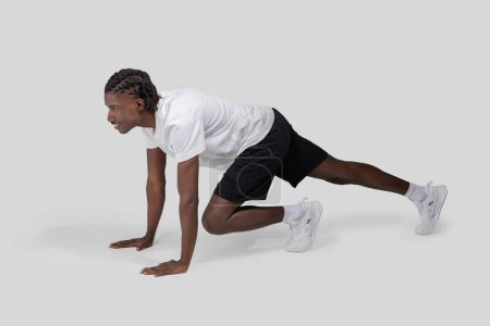 Foto de Una poderosa representación de un atleta negro en una posición inicial, preparado para correr, sobre un fondo gris liso que enfatiza la preparación y la fuerza - Imagen libre de derechos