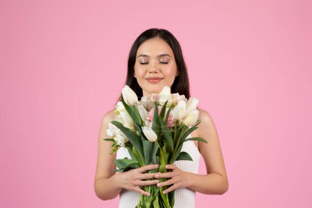 A lady is intimately interacting with a bouquet, showcasing european summer vibes Isolated on pink, she represents Generation Zs appreciation for nature