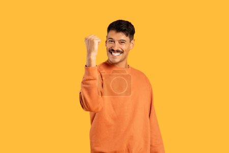 Téléchargez les photos : Un homme heureux souriant d'un poing fermé dans un geste de succès ou d'excitation sur fond de studio jaune - en image libre de droit