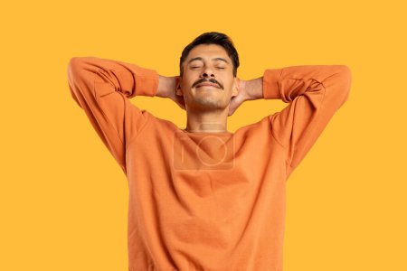 Hombre con bigote en prenda naranja estirando los brazos detrás de la cabeza, señalando un momento de descanso o relajación