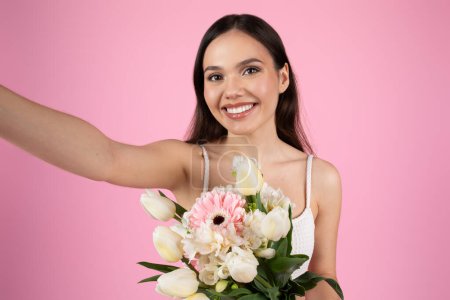 A joyful lady snaps a selfie, her face framed by a summer bouquet. Reflecting the carefree spirit of Generation Z, isolated on pink