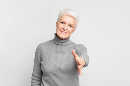 Photo for A senior European woman extends her hand in a friendly handshake against a white backdrop, highlighting the concept of s3niorlife engagement - Royalty Free Image