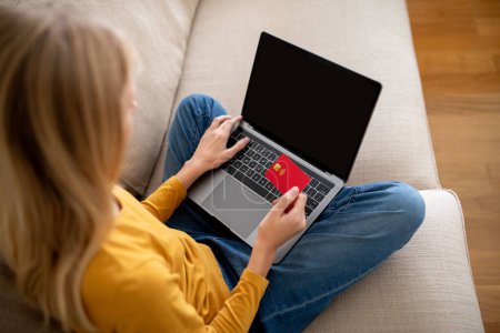 Foto de Chica adolescente usando el ordenador portátil con pantalla en blanco y tarjeta de crédito mientras está sentado en el sofá en casa, Mujer Adolescente Compras en línea, Hacer compras en Internet, Burla - Imagen libre de derechos
