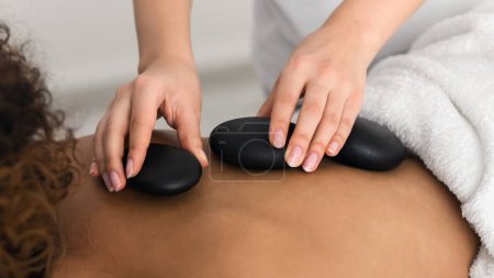 Téléchargez les photos : Masseur plaçant la pierre sur le dos de la femme pour effectuer un massage aux pierres chaudes, gros plan - en image libre de droit