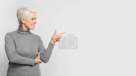 Foto de Una elegante mujer europea de alto nivel sonríe mientras hace gestos a su derecha, su pose encarna la vitalidad de s3niorlife con un toque moderno - Imagen libre de derechos