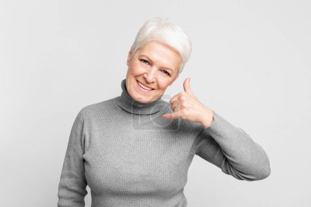 Photo for Friendly senior european woman displays a call me hand gesture, suitable for s3niorlife communication themes - Royalty Free Image