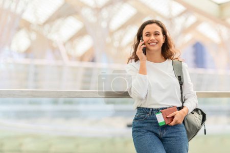 Téléchargez les photos : Femme souriante marchant et parlant sur son téléphone portable à l'aéroport, jeune femme heureuse profitant d'une conversation mobile agréable tout en allant à la porte d'embarquement à l'aérogare, Copier l'espace - en image libre de droit