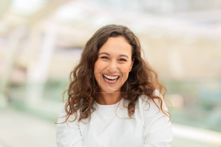Photo for Radiant Beautiful Woman Laughing At Camera While Standing At Airport Terminal, Portrait Of Beautiful Young Female With Curly Hair And Cheerful Smile, Closeup Shot, Copy Space - Royalty Free Image